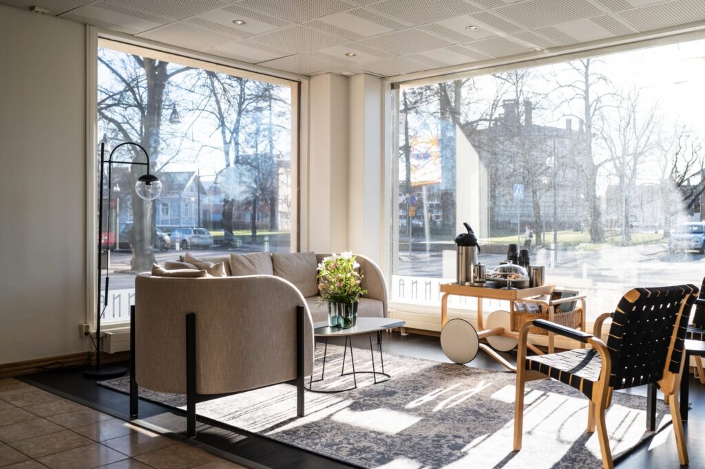 Hotellin aula-alue suurilla ikkunoilla, sohva ja kahvitarjoilu auringonvalossa.