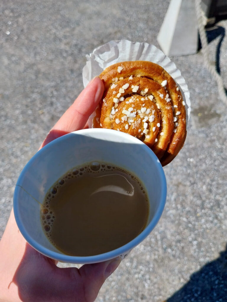 Kahvikuppi ja korvapuusti kädessä aurinkoisena päivänä Raumalla.