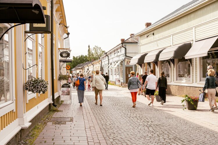 People walking along a cobblestone street in Old Rauma between historic wooden buildings on a sunny day.