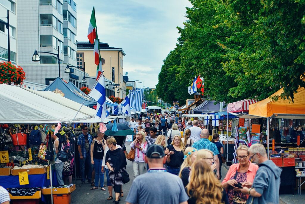 Vilkas markkinatunnelma Raumalla, jossa ihmiset liikkuvat kojujen ja lippujen täyttämällä kadulla.