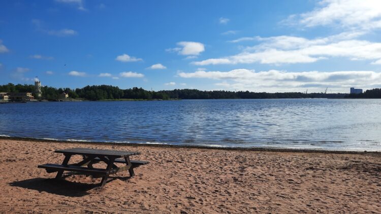 Hiekkaranta ja piknikpöytä meren rannalla aurinkoisena päivänä Raumalla.