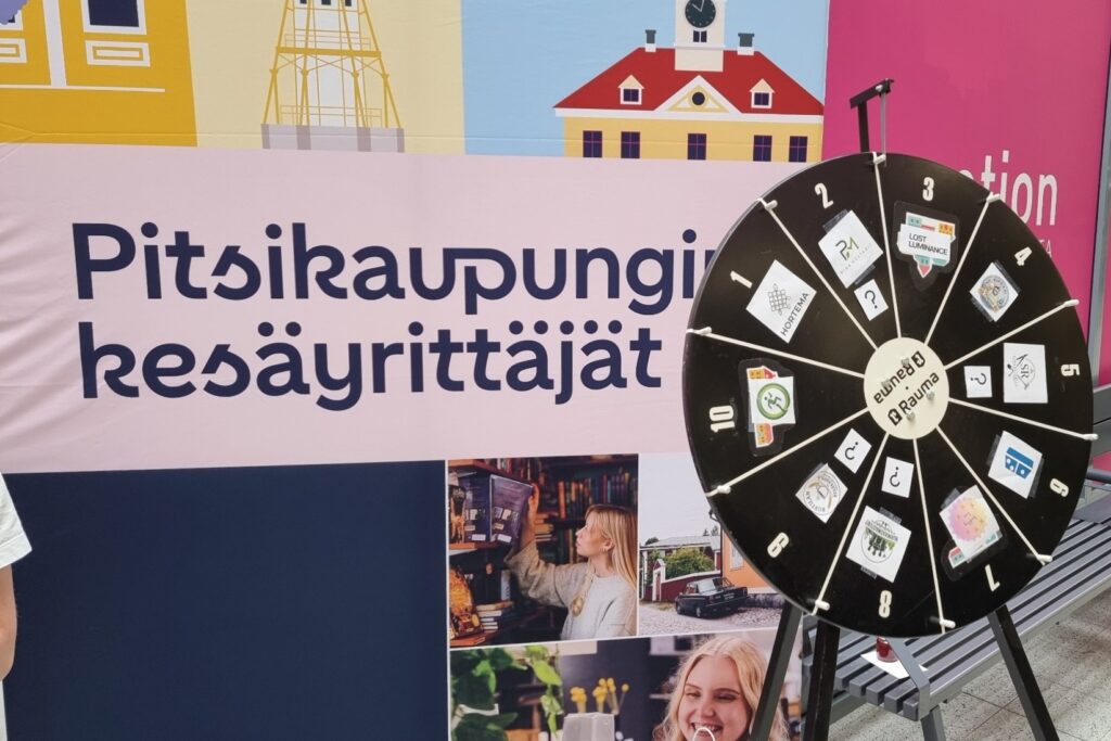 Pitsikaupungin kesäyrittäjien esittelypiste ja yritysten logoilla varustettu arvontapyörä kauppakeskuksessa Raumalla.